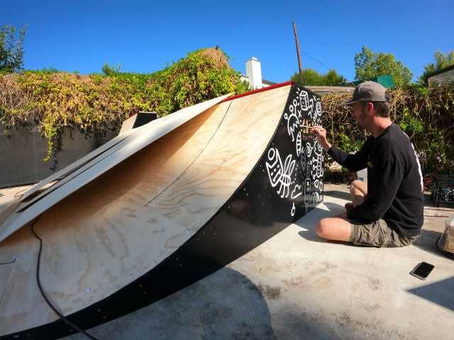 Artist adding white graphics to the black side of an OC Ramps wooden quarter pipe