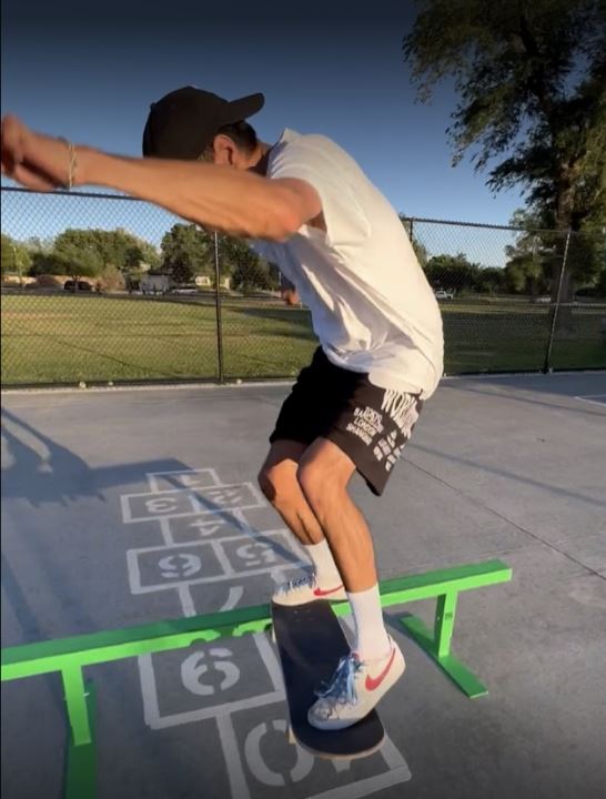 Skateboarder riding the green OC Ramps flat rail on an outdoor concrete court