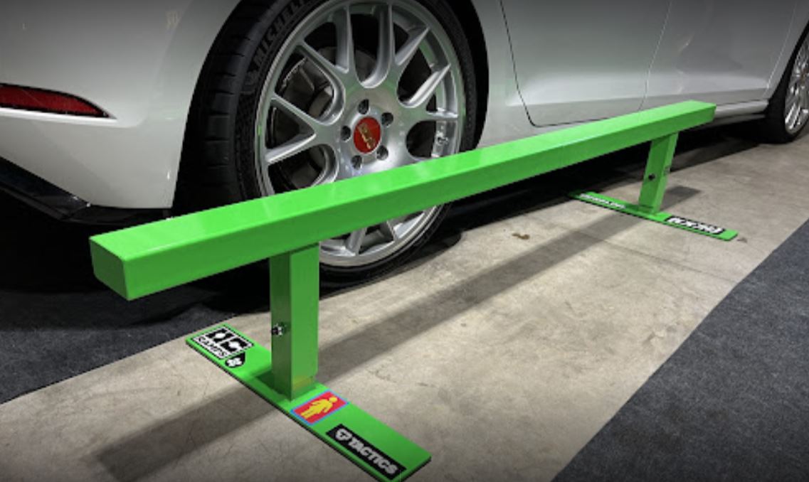 Green Monster flat skate rail showing its support posts and wide base feet beside a parked car
