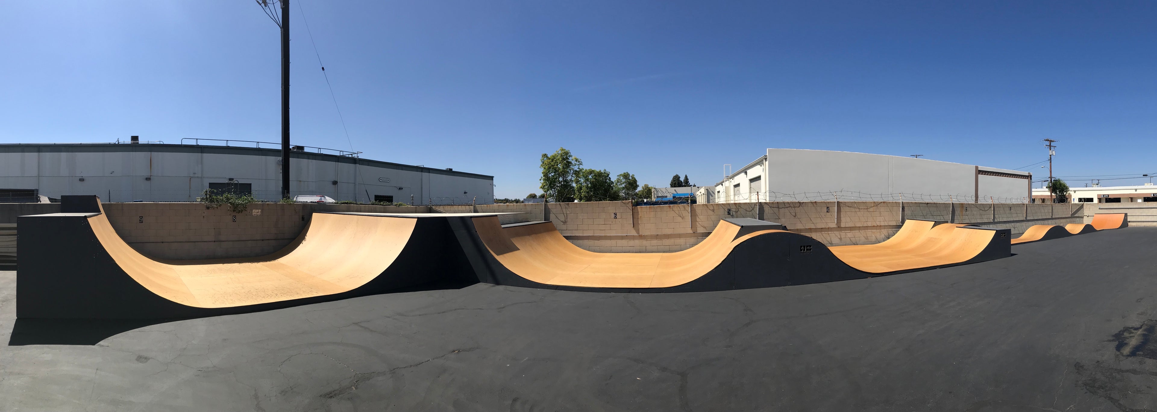 Long row of wood transition ramps and skate obstacles in a paved industrial yard.