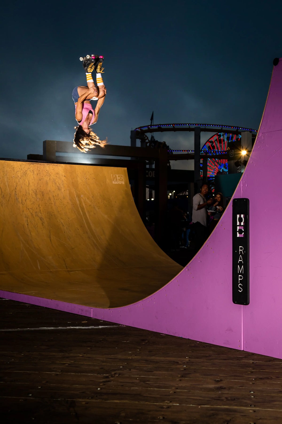 A skateboarder in a pink outfit performs an aerial backflip on a large wooden halfpipe ramp at EA Skate 4