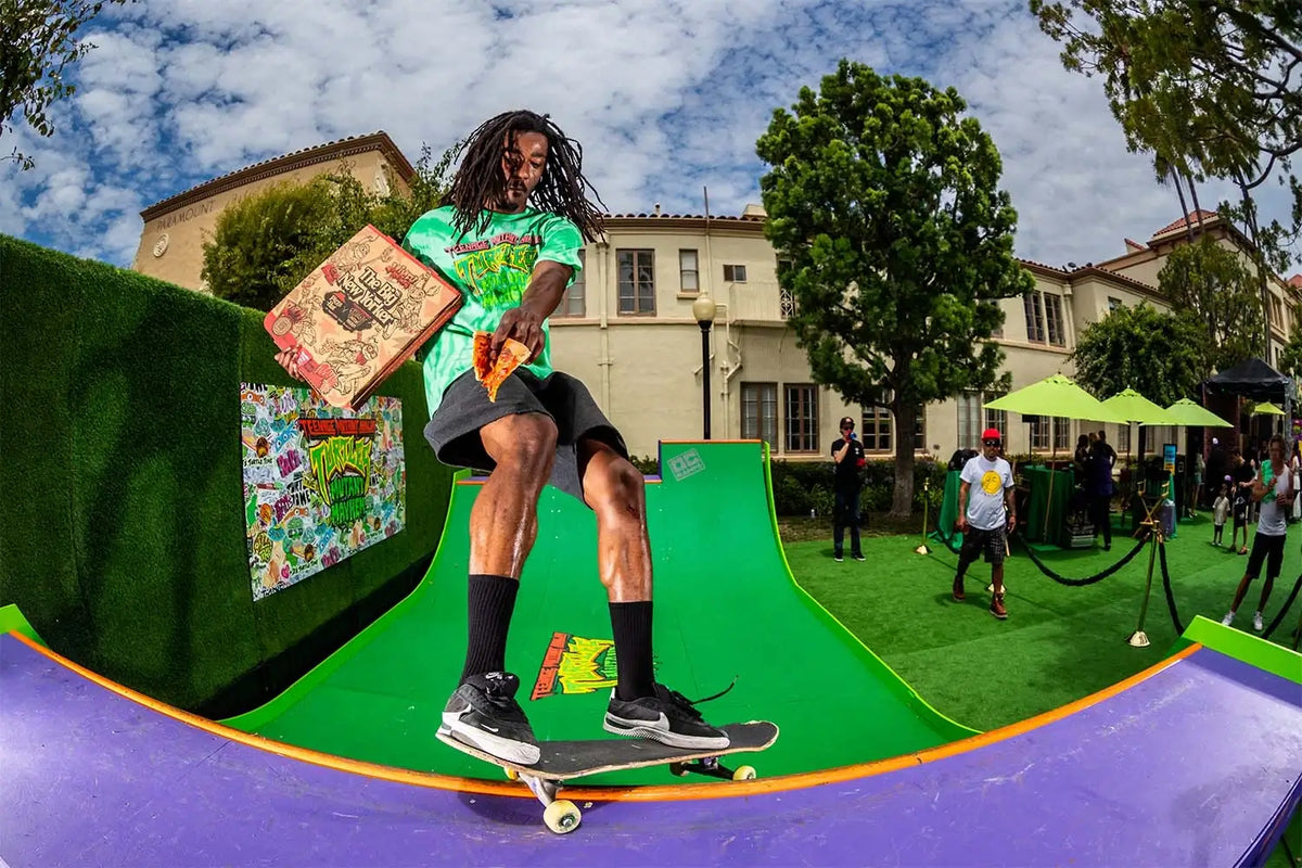 A skateboarder in a green graphic t-shirt and black shorts rides a skateboard on a green ramp at FuelFest 2024