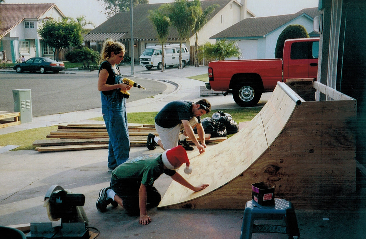 Three people assembling a wooden quarter pipe in a driveway