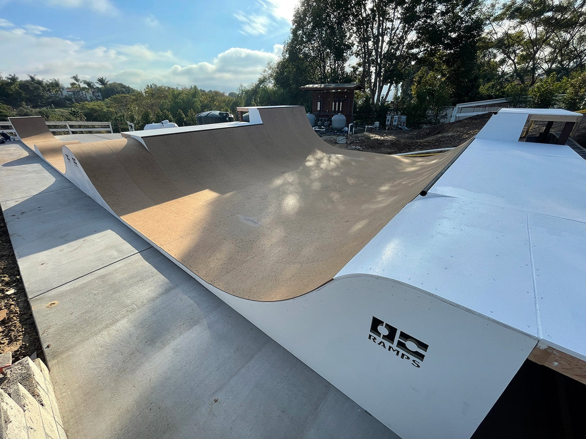 A curved concrete skate bowl ramp with a light brown paper liner and white outer walls