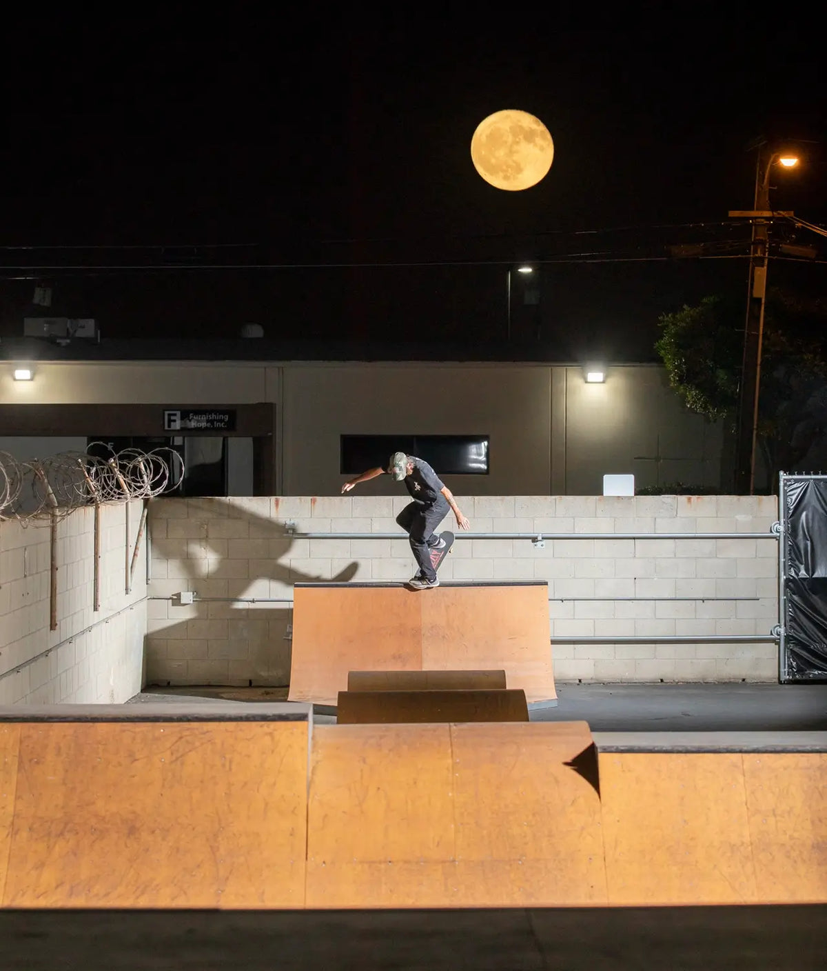 A skateboarder performs a trick on a wooden ramp at a skatepark at night, at OC Ramps's event space