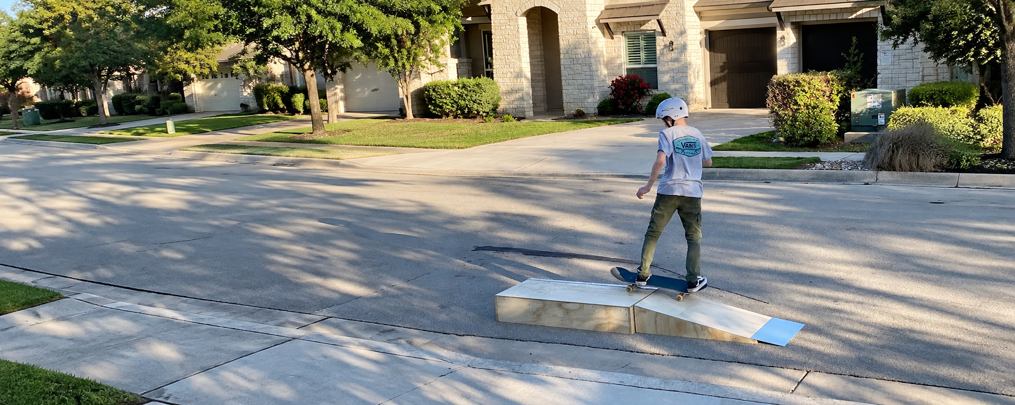 Young skater using a box and kicker setup outside a home
